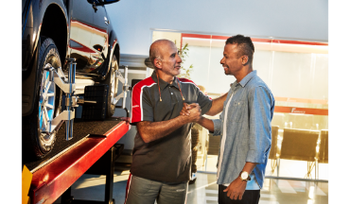 Mecânico de automóveis aperta a mão de um cliente em uma oficina mecânica ao lado de um carro.