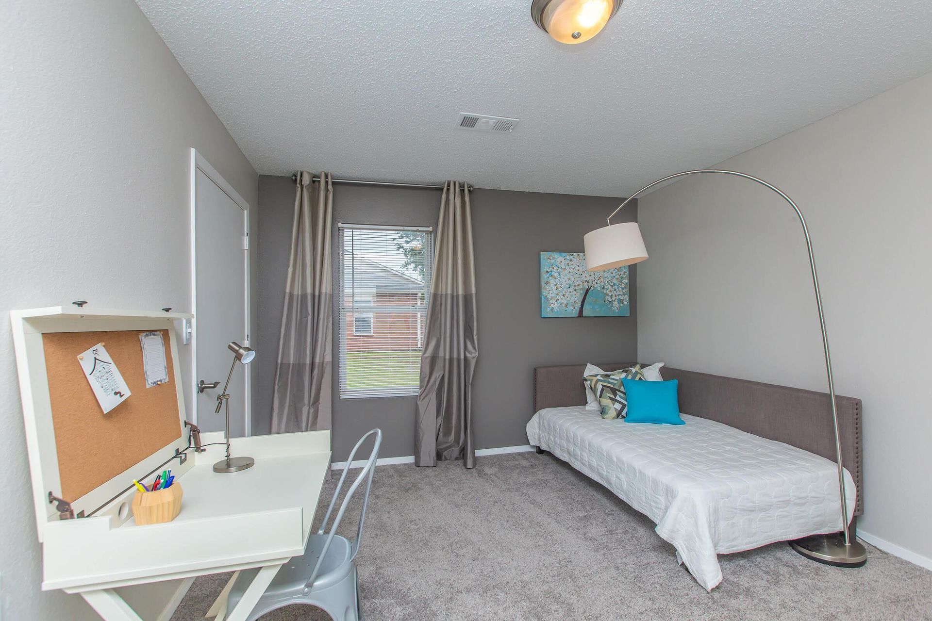A bedroom with a bed, desk, lamp, and window at 51 at Southaven Apartment Homes in Southaven, MS.