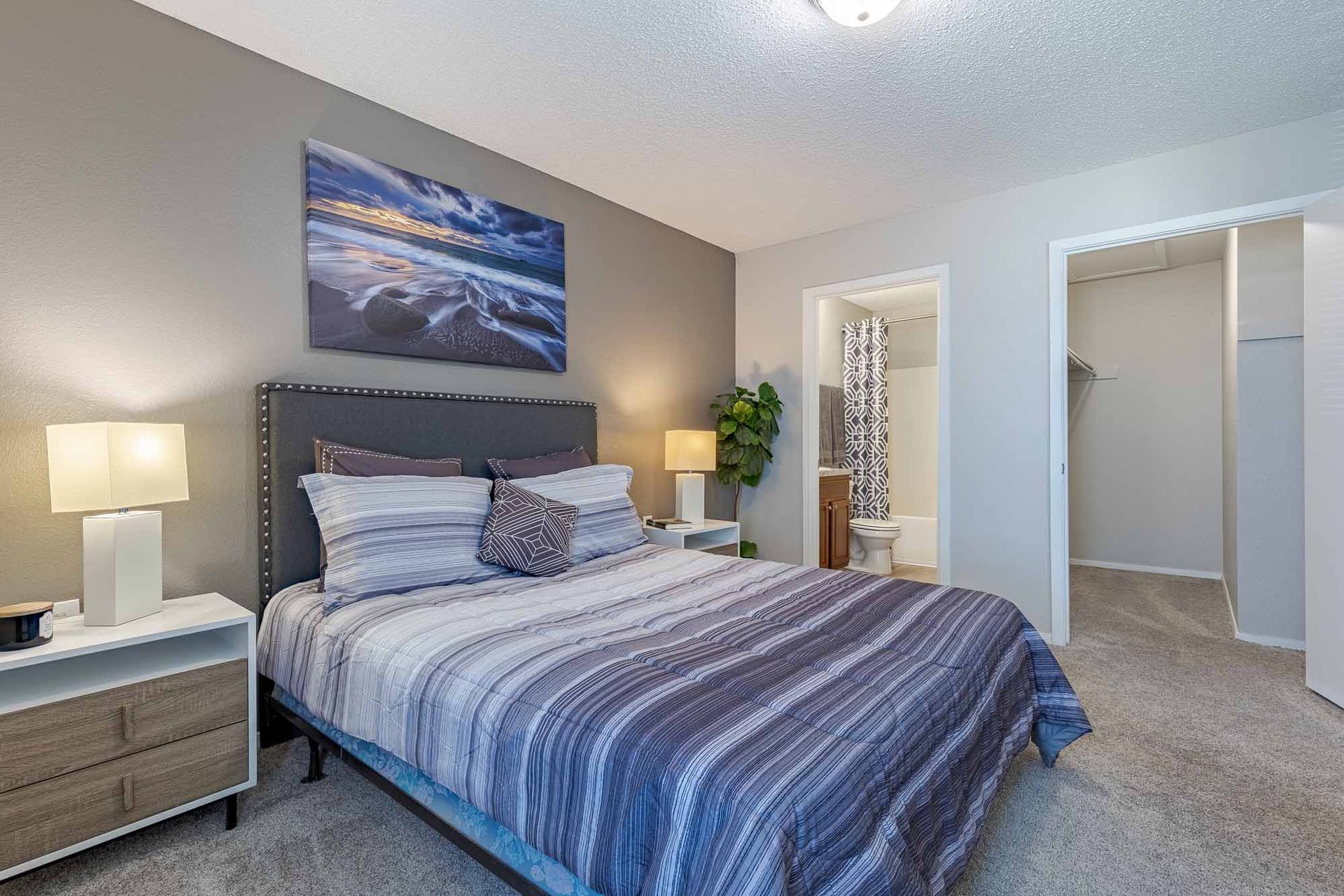 Bedroom with bed, bedside tables, art, window, and dresser. Gray walls, striped bedding, and carpet.