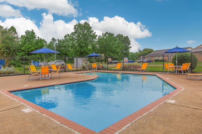 Pool area with blue water, orange chairs, umbrellas, and trees.