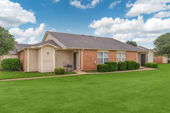 Row of brick and beige apartments with green lawn under blue sky.