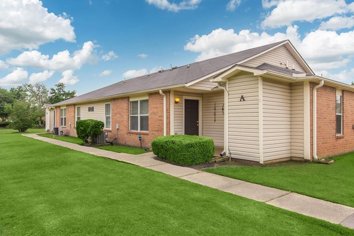 Two-story brick and siding duplex with green lawn and blue sky.