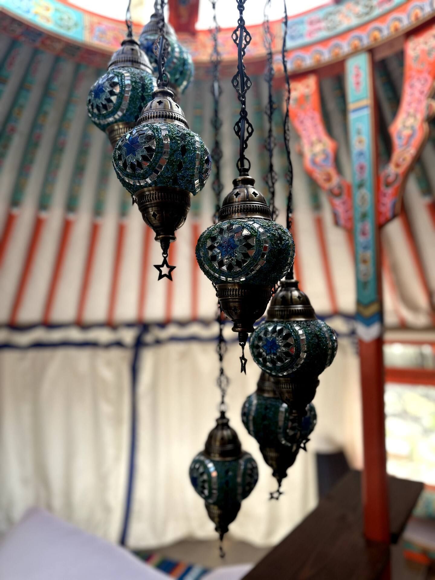 Hanging teal mosaic lanterns inside a yurt with colorful wooden frame details.