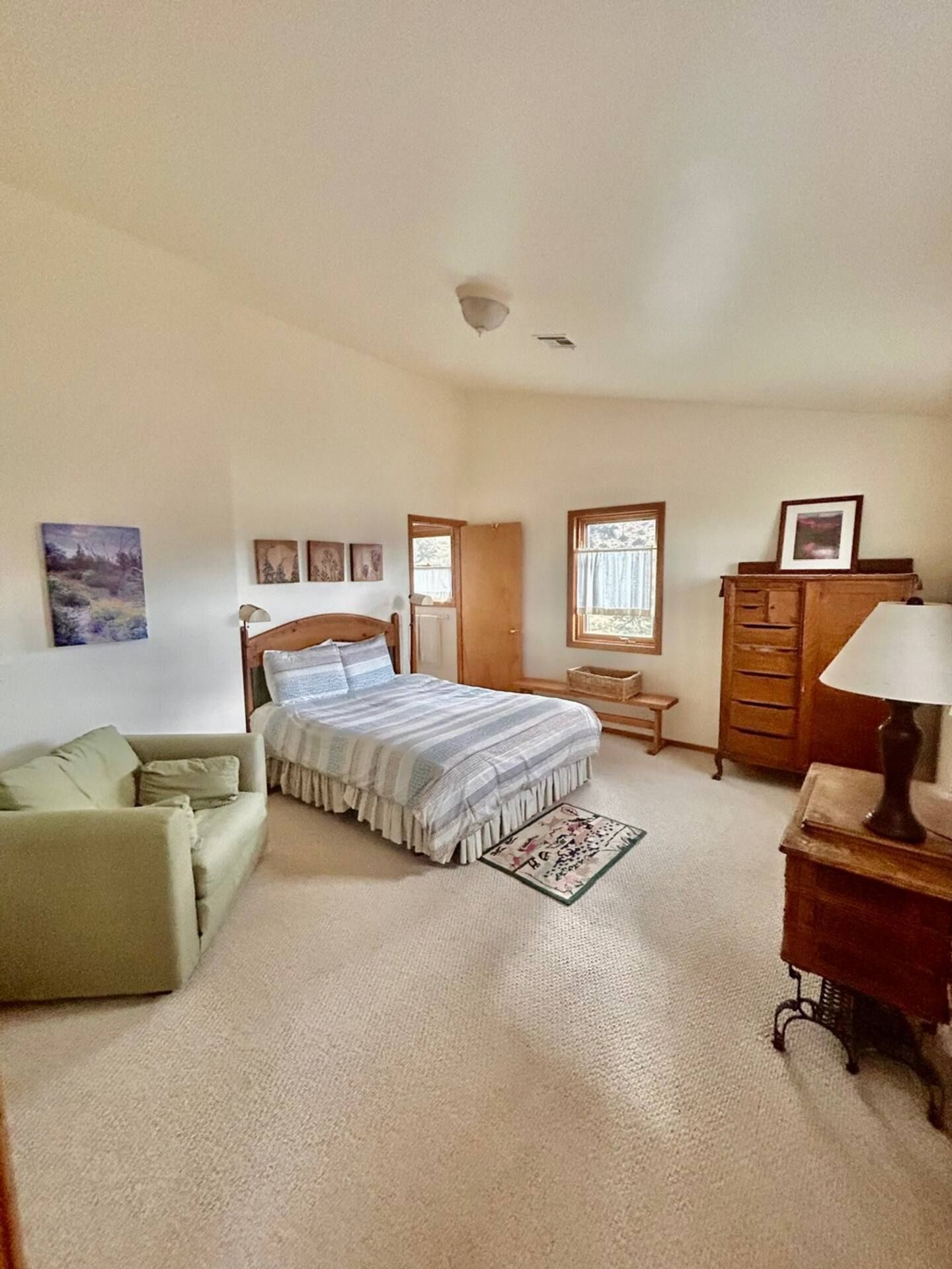 Bedroom with bed, sofa, dresser, rug, and small window. Off-white walls and light-colored carpet.