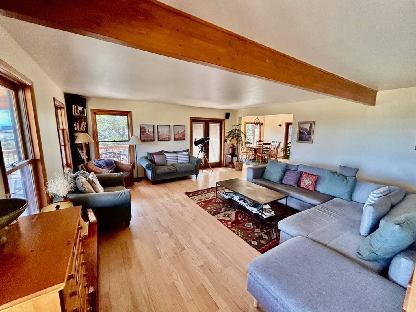 Spacious living room with hardwood floors, a gray sectional sofa, and wooden beams on the ceiling.