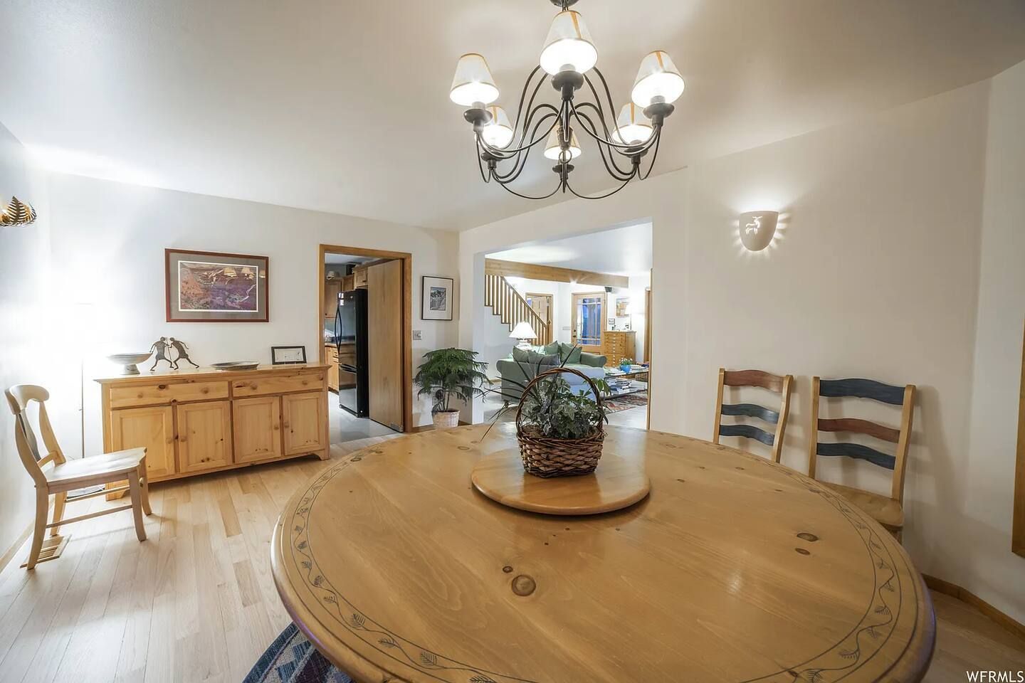 Dining room with a wooden round table, chandelier, and a view into another room.