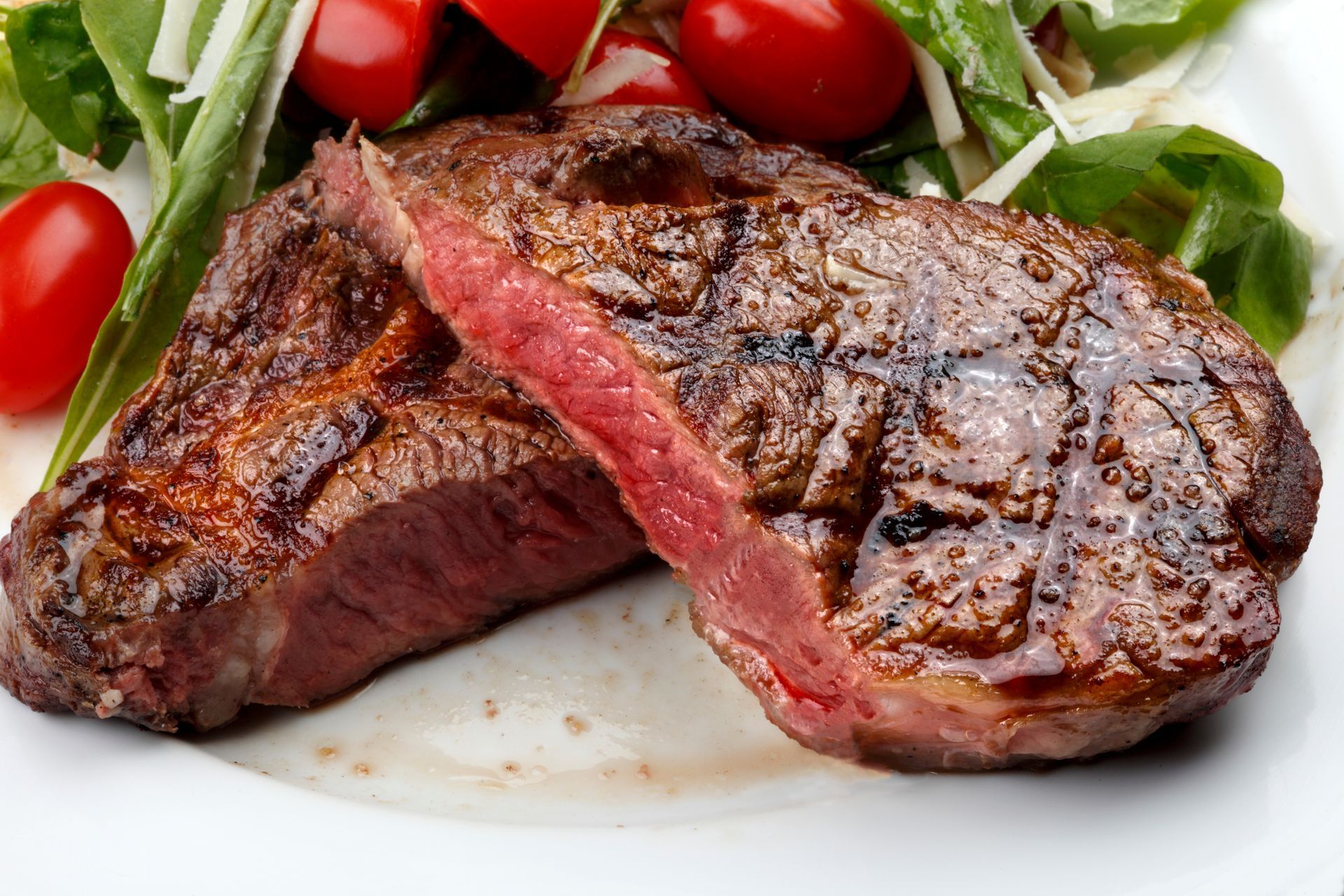 Grilled steak cut open, revealing pink interior, served with salad and tomatoes.