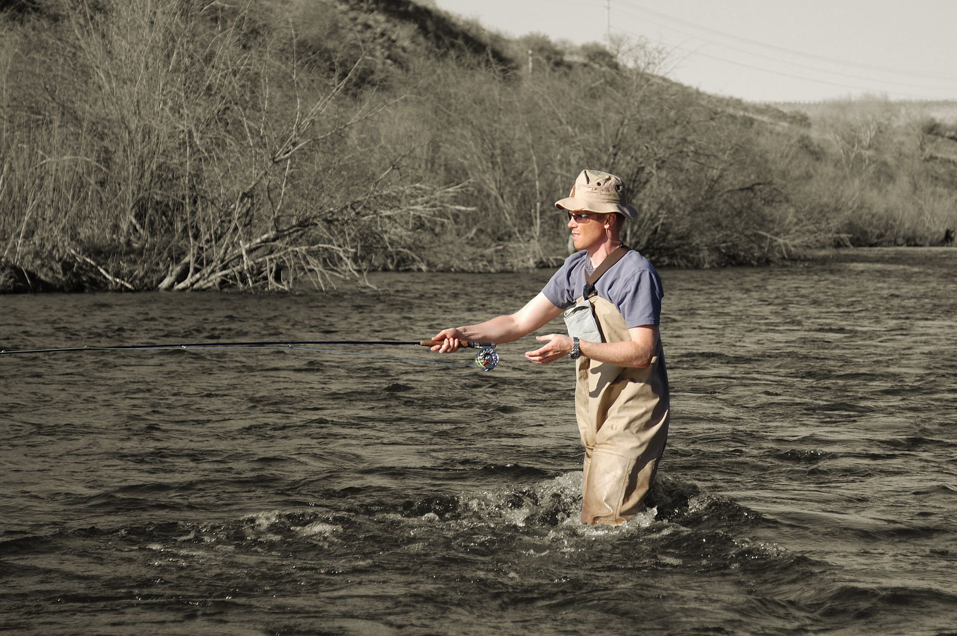 Person fly fishing in a river, wearing waders.