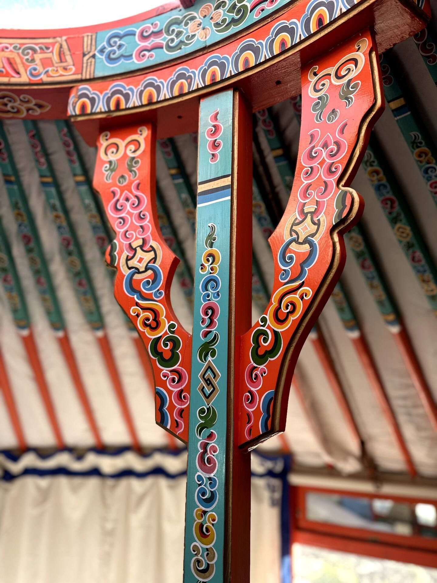 Close-up of a brightly painted interior pole with red, blue, and yellow floral patterns in a yurt.