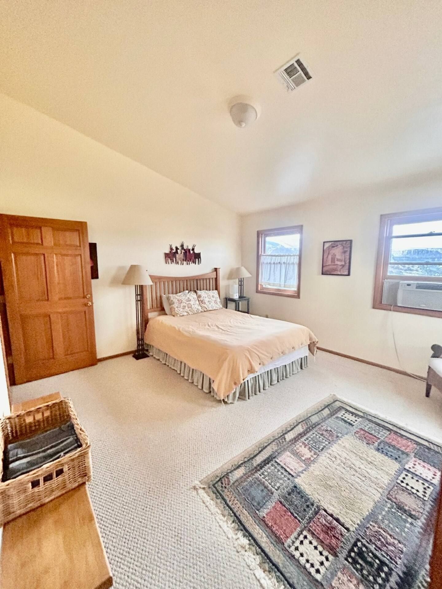 Bedroom with bed, rug, and wooden door. Neutral tones, two windows with mountain views.
