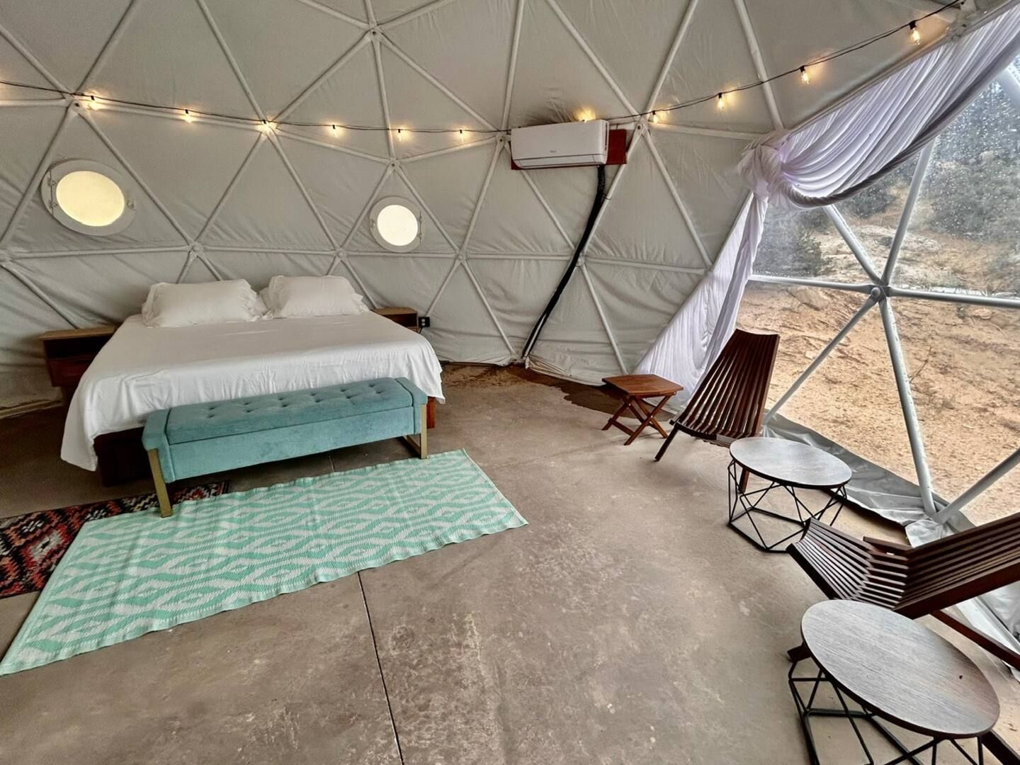 Interior of a dome-shaped lodging with a bed, bench, rug, chairs, and two small tables.