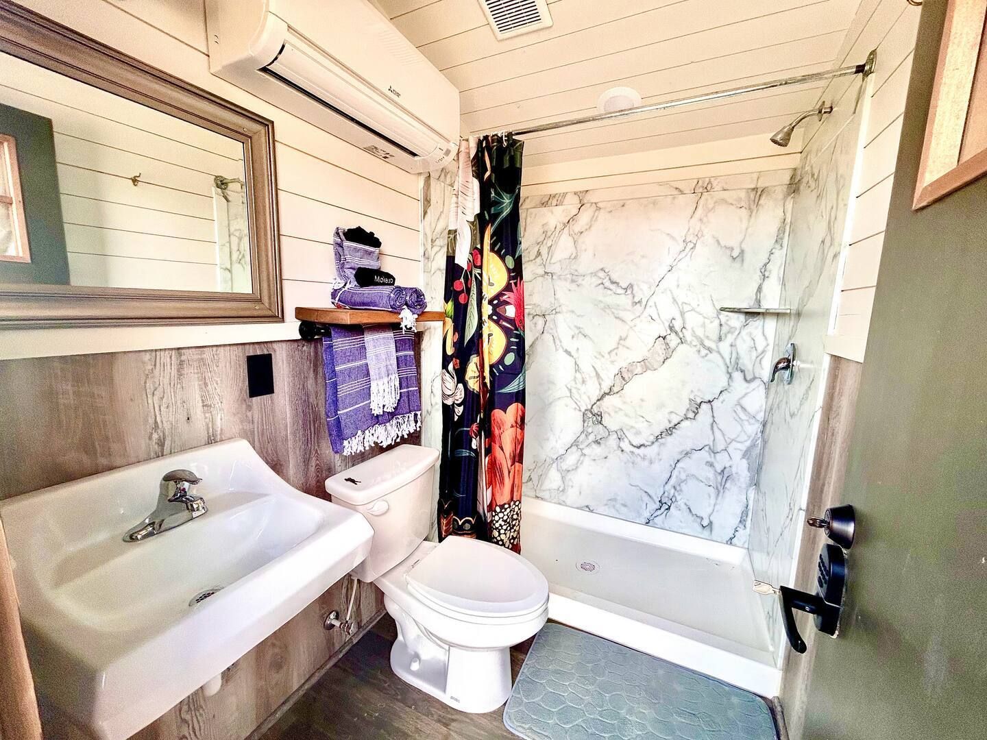 Bathroom with sink, toilet, and shower. White walls, wood accents, and colorful shower curtain.