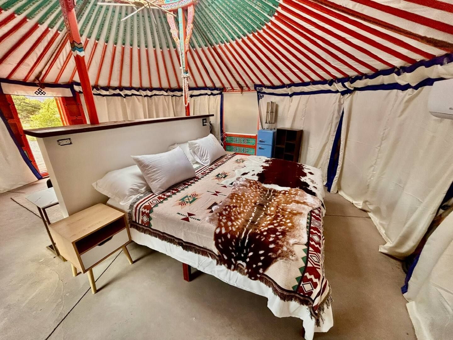 Interior of a yurt with a bed, small nightstand, and colorful roof.