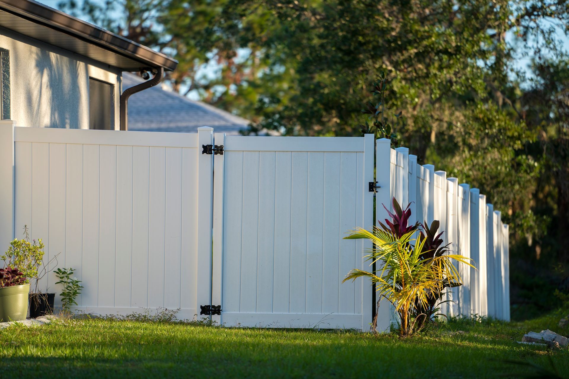 White fence with a gate, green grass, and a house in the background.