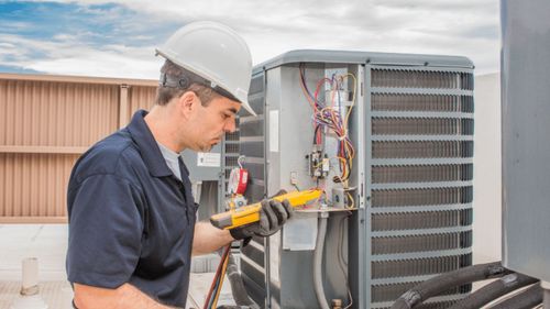 HVAC technician in hard hat, using a multimeter on an air conditioner unit.