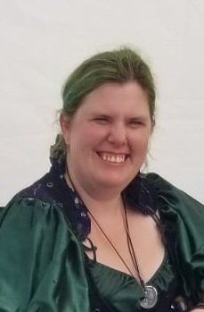 A woman with green hair is wearing a green dress and smiling, Britteny.