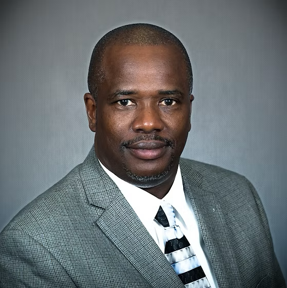 Man in a gray suit and patterned tie, smiling, indoors.