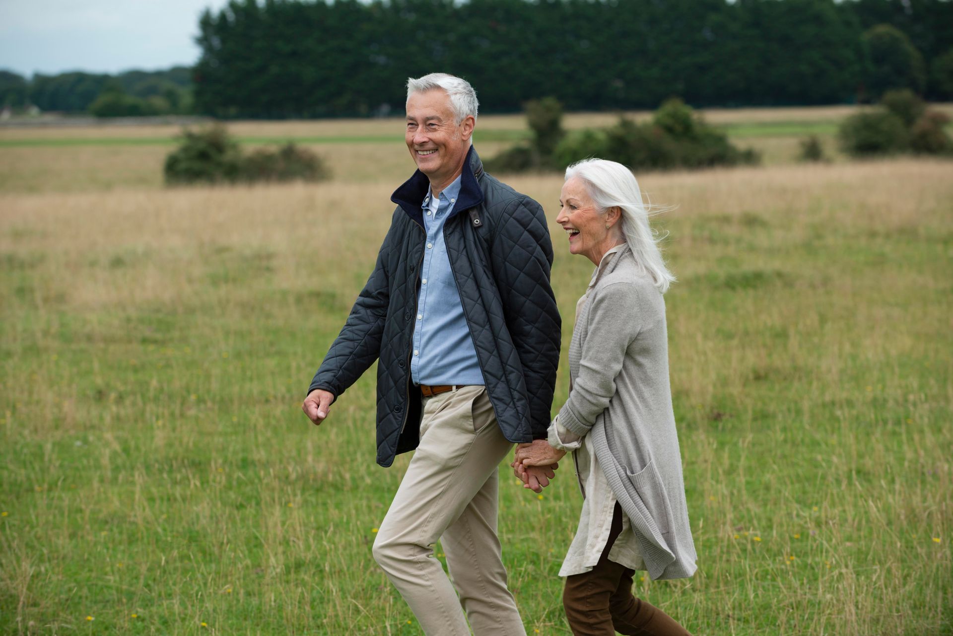 A smiling older couple holding hands, walking in a grassy field.