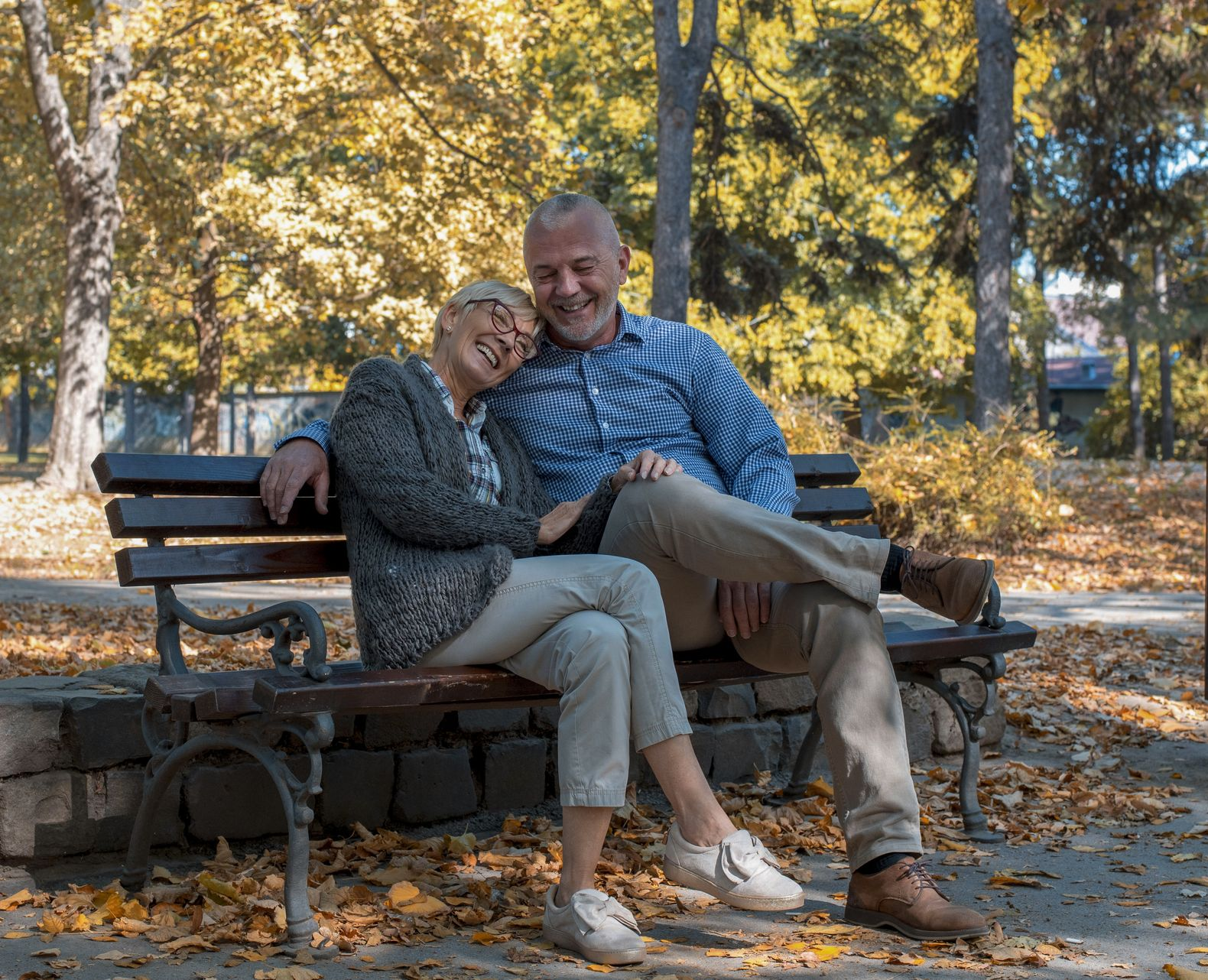 Couple sitting on park bench, smiling, surrounded by autumn leaves.