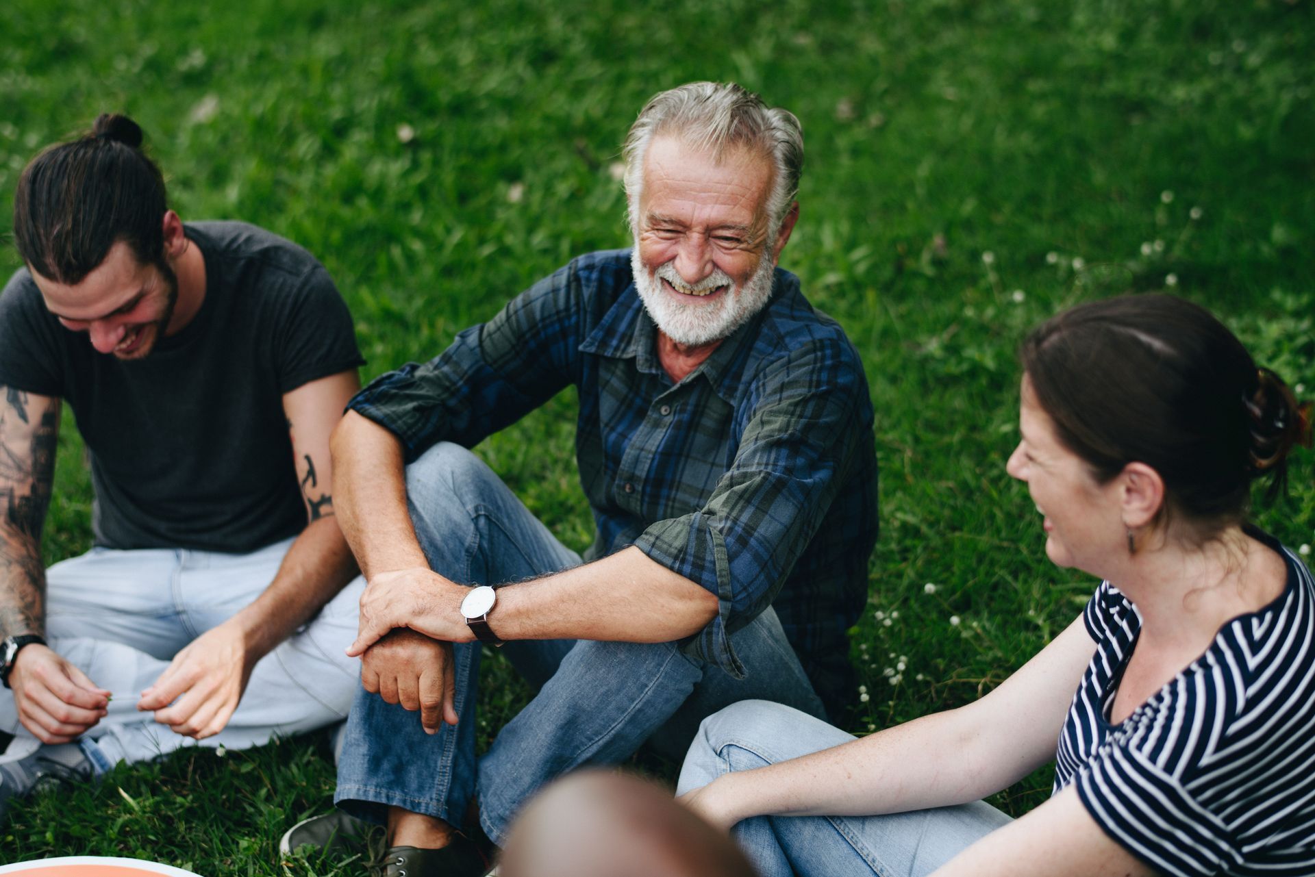 Three people laughing while sitting on grass outdoors.