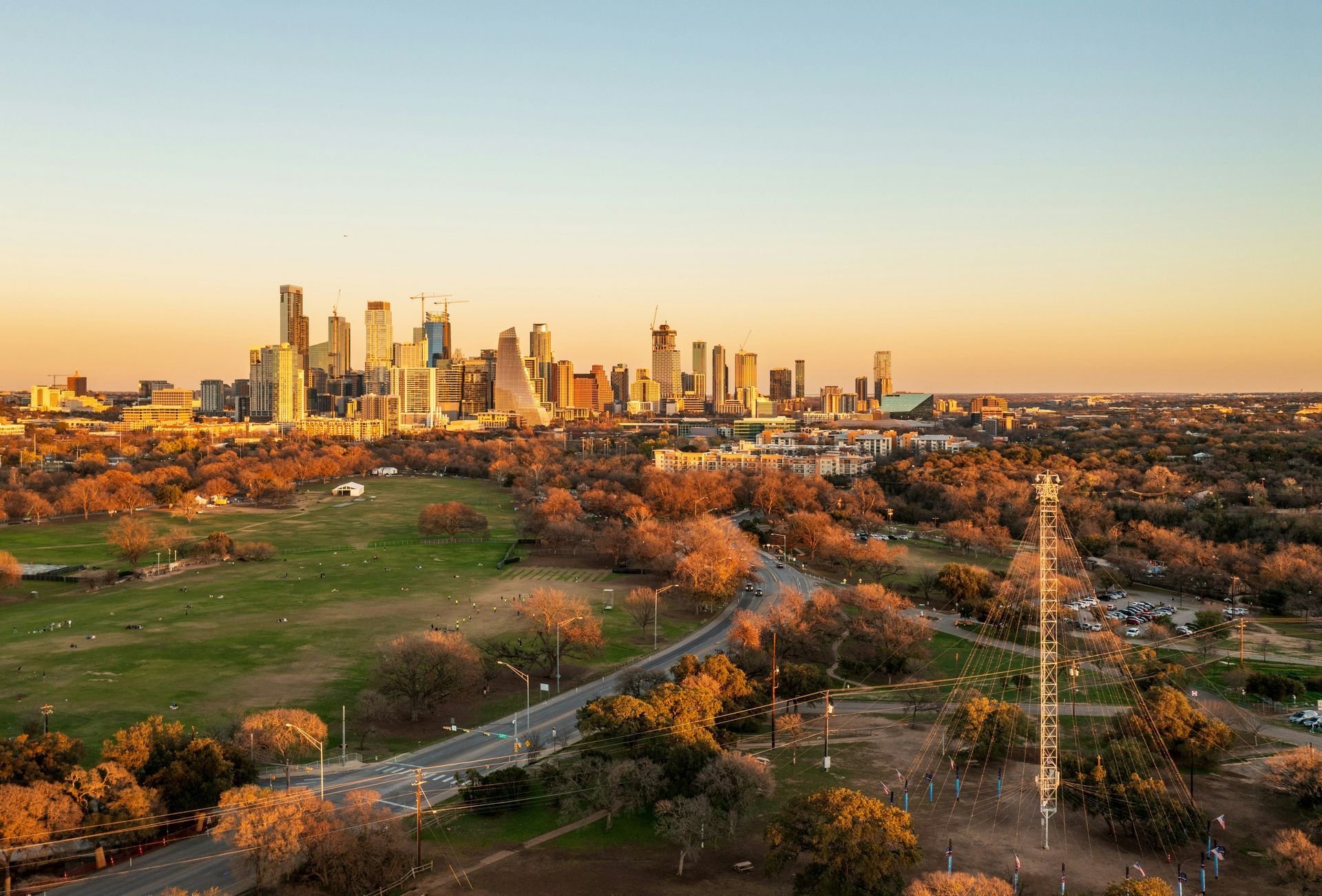 City skyline at sunset over a park with a winding road and communication tower.