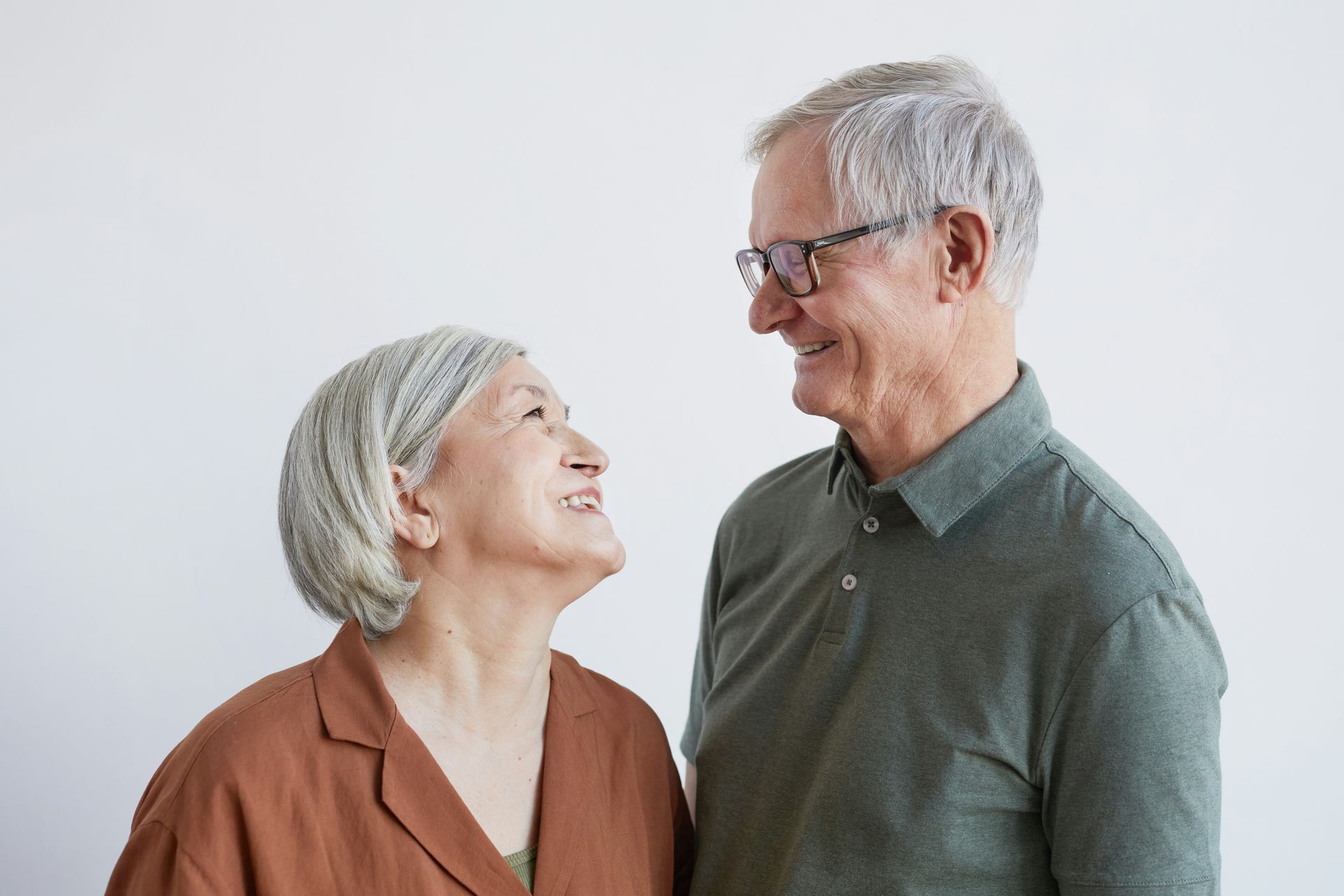 Smiling older couple looking at each other, against a white background.