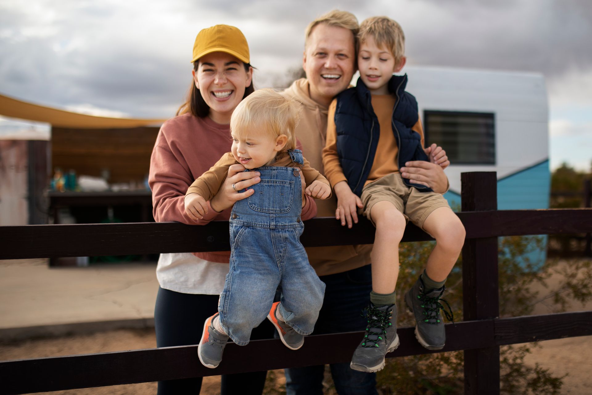 Family of four smiles together outdoors, leaning on a fence.