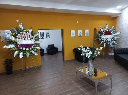 Pequeña sala de recepción con paredes naranjas, guirnaldas florales, asientos oscuros y una mesa de centro de cristal.