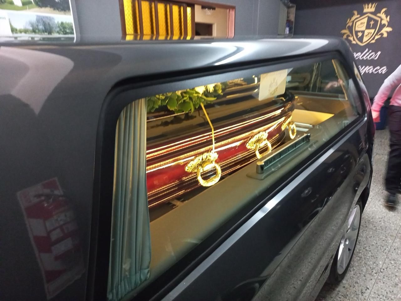 Coche fúnebre negro decorado con ataúd adornado con oro visible a través de la ventana lateral.