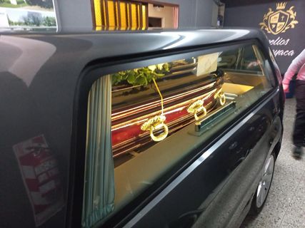 Coche fúnebre negro decorado con ataúd adornado con oro visible a través de la ventana lateral.