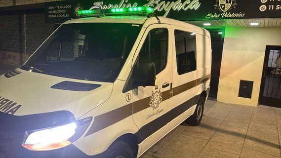 Una ambulancia blanca con luces verdes intermitentes estacionada frente a un edificio por la noche.