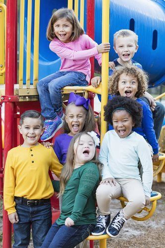 A diverse group of seven children with joyful expressions sitting together on playground equipment.