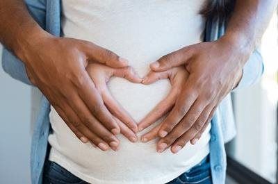 Hands form a heart shape over a pregnant abdomen.