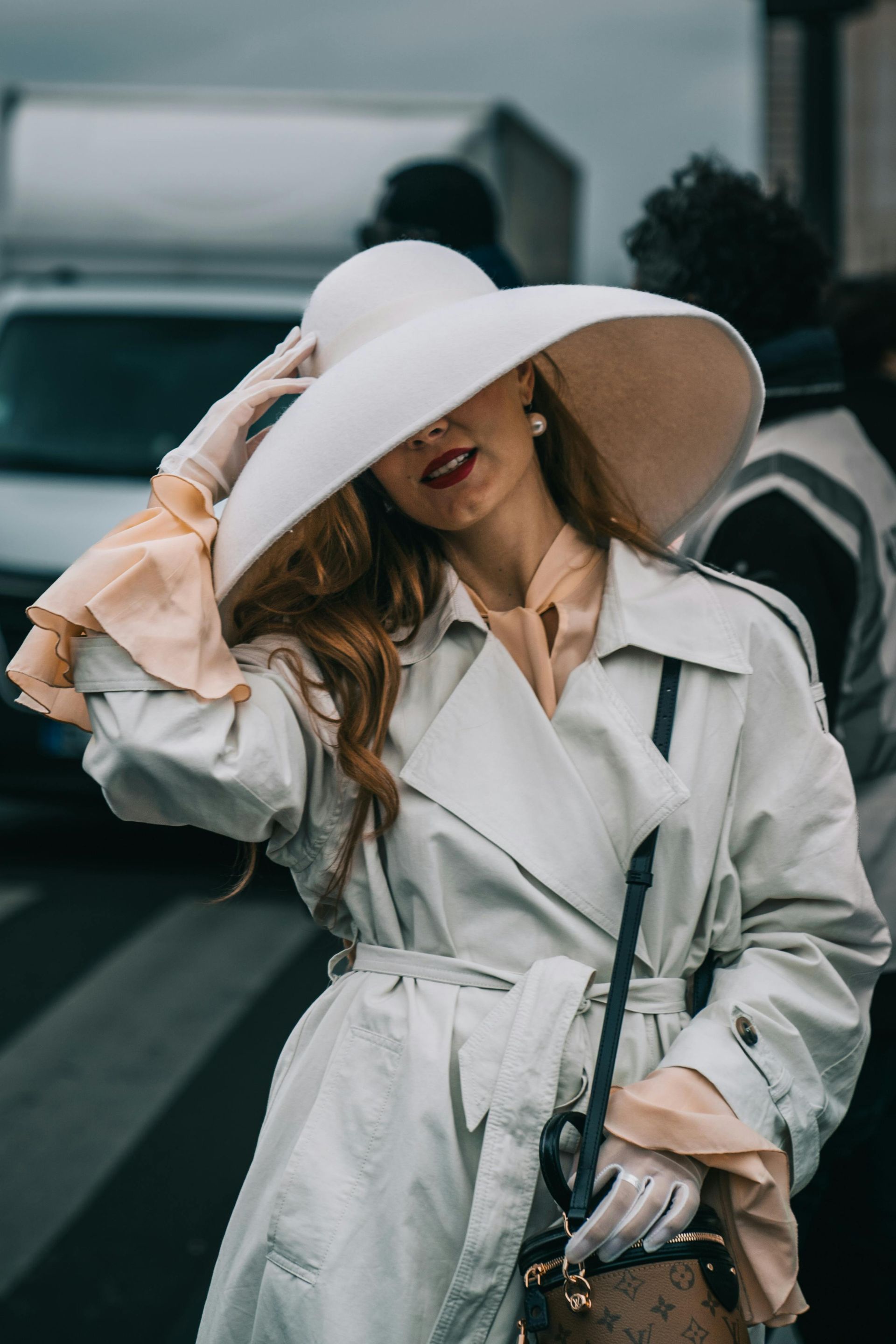 A woman wearing a white hat and gloves is standing on a street.