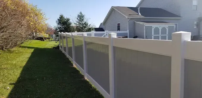 A white and gray privacy fence along a green lawn, next to a house on a sunny day.