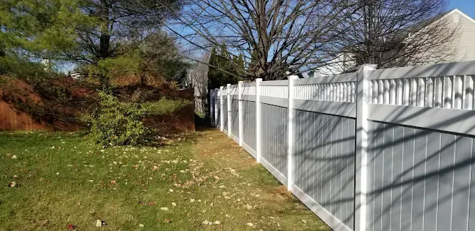 A white fence in a yard with green grass and bare trees.