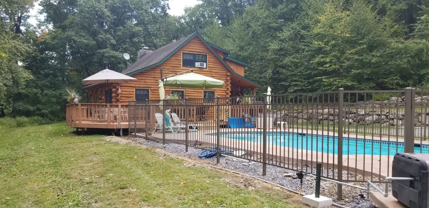 A log cabin with a deck, pool, and forest background.