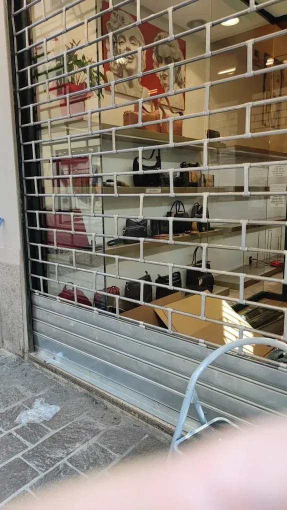 Una vetrina con un cancello di sicurezza metallico chiuso. All'interno, gli articoli sono visibili sugli scaffali e sul bancone.