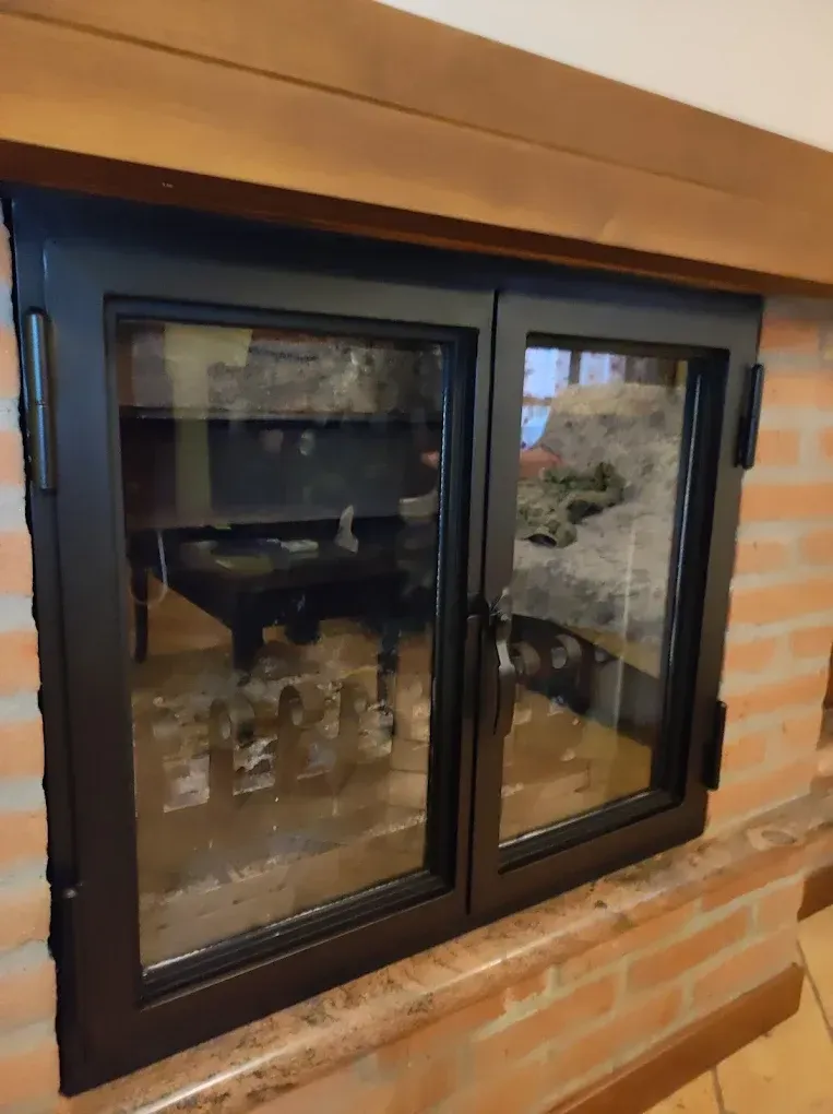 Porte del camino in vetro con cornice nera incastonate nei mattoni.