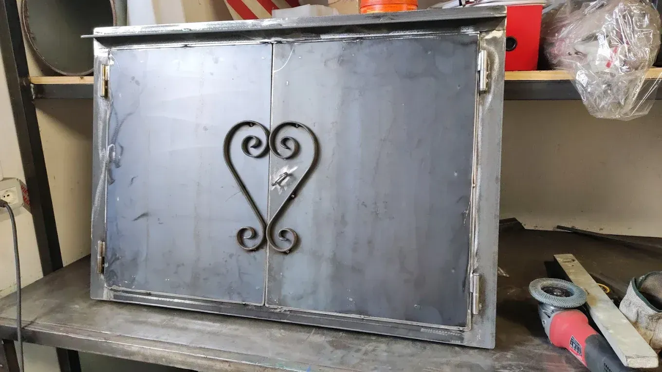 Mobiletto in metallo con doppie ante e cuore decorativo sulla parte anteriore.