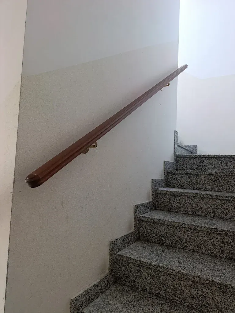 Corrimano marrone su una parete color crema sopra le scale in granito.