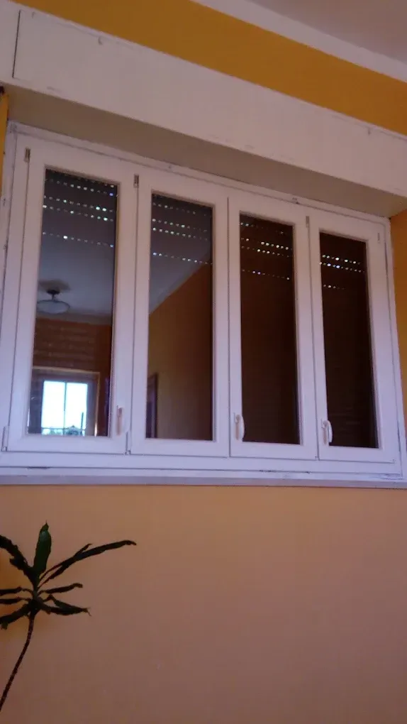 Finestra bianca con quattro vetri incastonati in una parete gialla, riflesso dell'interno visibile, pianta in basso.