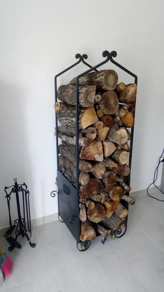 Portalegna in metallo nero pieno di legna da ardere, su ruote, accanto a un set di attrezzi per camino.