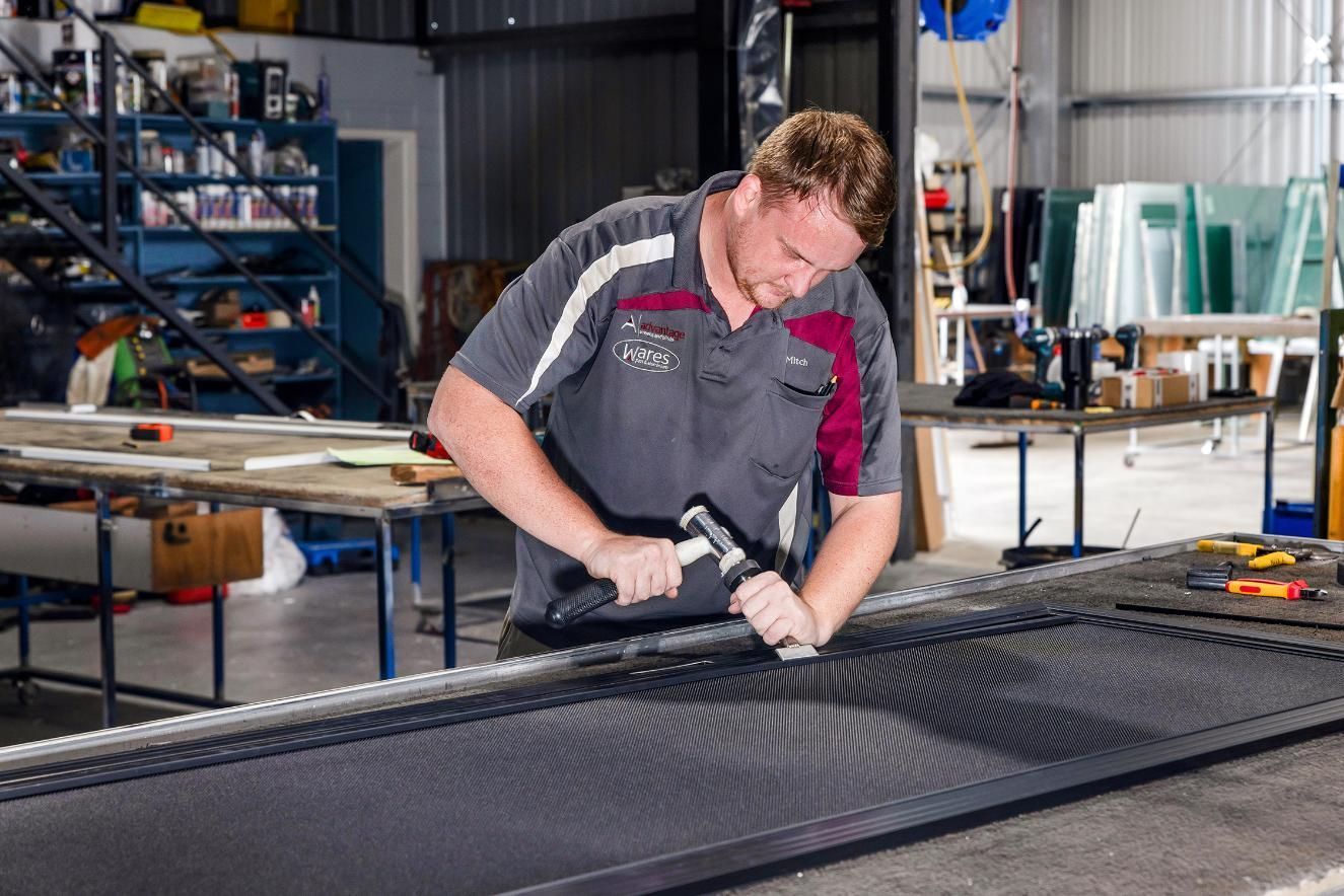 A Man Is Working On A Piece Of Metal In A Factory — Wares Blinds, Screens & Awnings In Gladstone Central, QLD