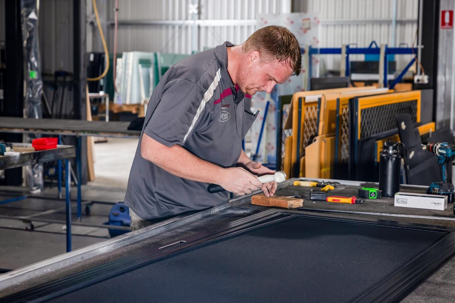 A Man Is Working On A Piece Of Metal In A Factory — Wares Blinds, Screens & Awnings In Gladstone Central, QLD