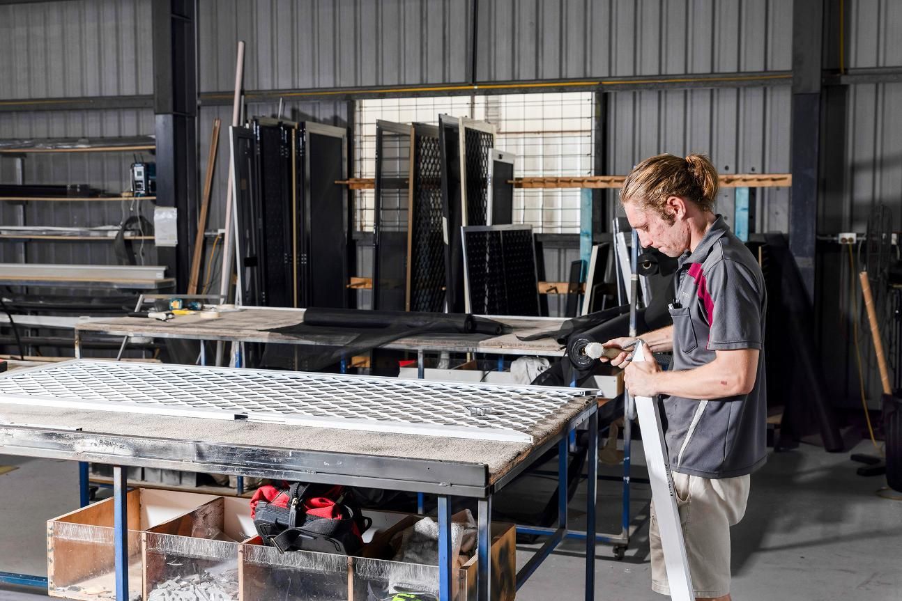 A Man Is Working On A Piece Of Metal In A Factory — Wares Blinds, Screens & Awnings In Gladstone Central, QLD