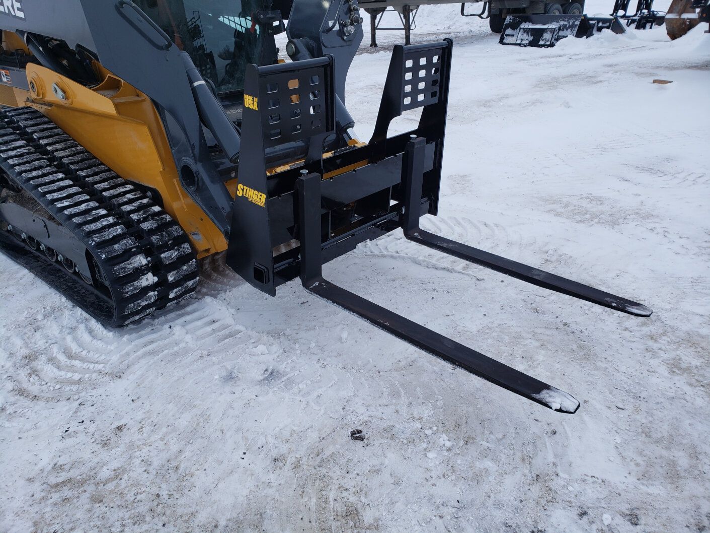 Stinger skid steer pallet fork attachment on track loader lifting materials in winter job site conditions