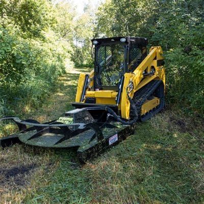 Skid steer loader operating Prime Attachments rigid deck brush mower clearing brush and vegetation along wooded trail