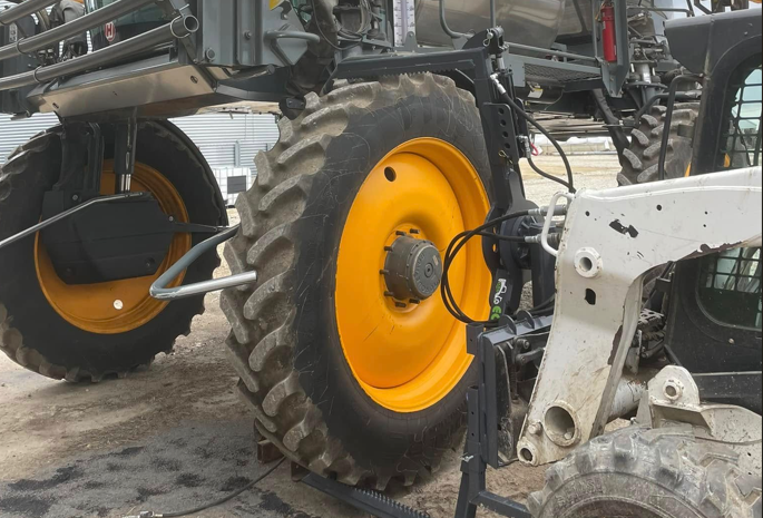 Skid steer removing sprayer tire showing safe tire change process with heavy equipment