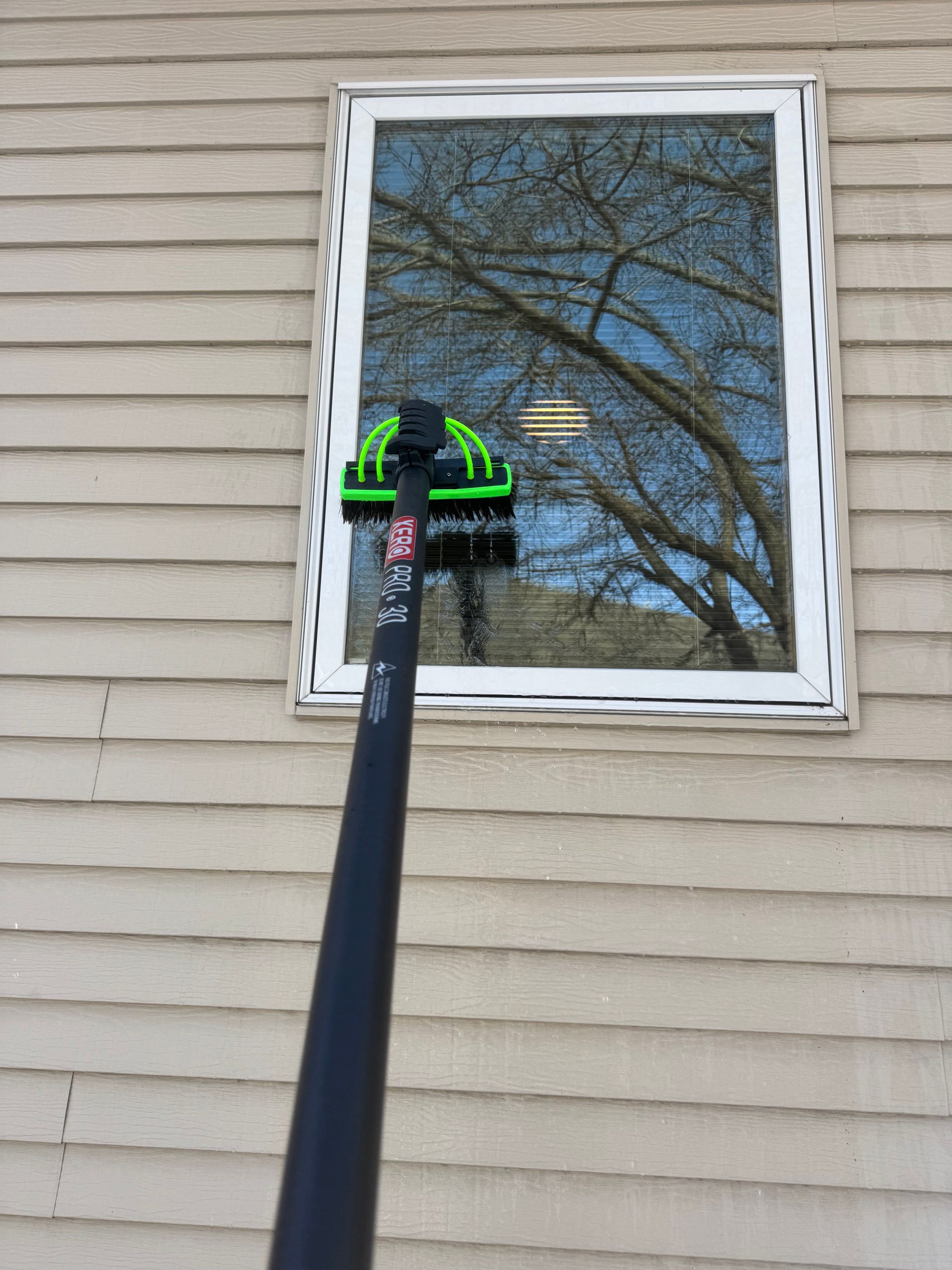 A window is being cleaned with a brush on a pole